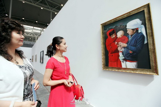 6月25日,一位观众在新疆国际艺术双年展上欣赏布面油画作品“欢乐”。