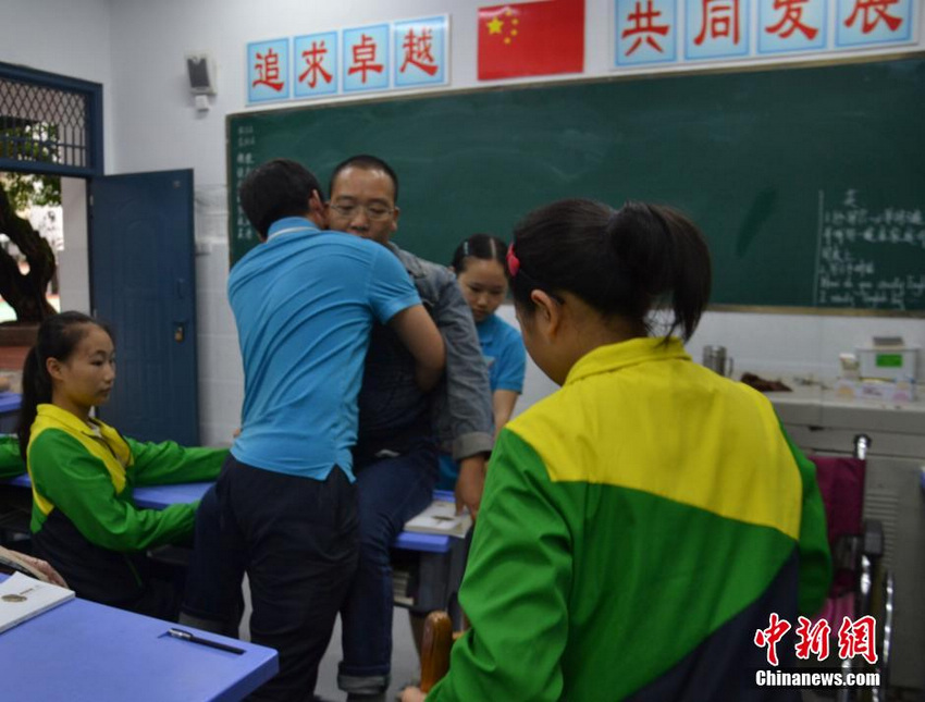 图为学生帮助詹光伟老师坐上课桌讲课。