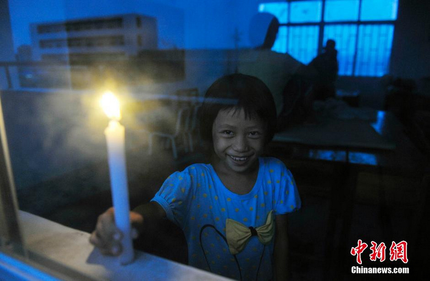 图为在文昌市罗豆农场中学安置点一位小朋友点起了蜡烛，脸上露出了笑容。