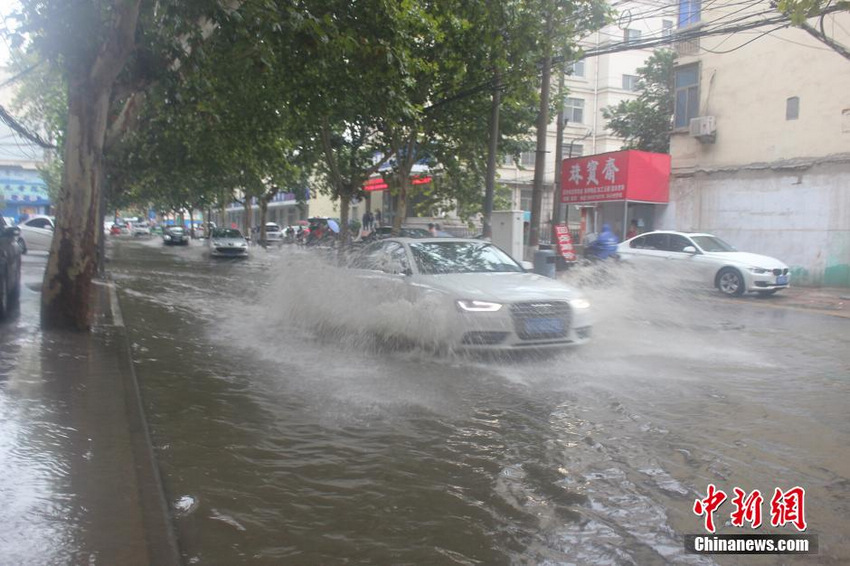 图为郑州市一处积水点，一辆轿车疾驰而过，水花四溅。