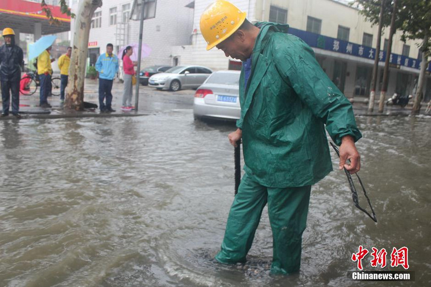 图为郑州陇海路与交通路交叉口积水蔓延，工作人员正在抓紧疏通排水口。