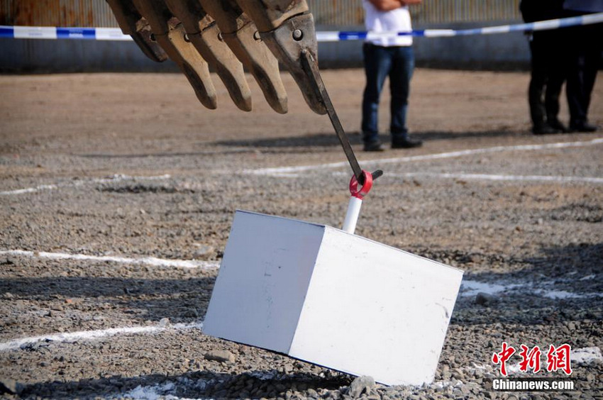 图为参赛者用挖掘机“爪子”上的挂钩将方铁块勾起。