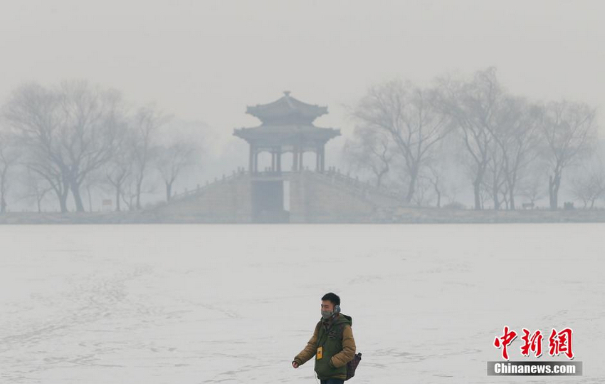 1月14日，一名戴着口罩的游客走在北京颐和园的昆明湖冰面上，冰面蒙上了2015年北京第一场雪，雾霾却将雪景掩盖，远处的景色难以辨清。当日，北京空气陷入重度污染。
