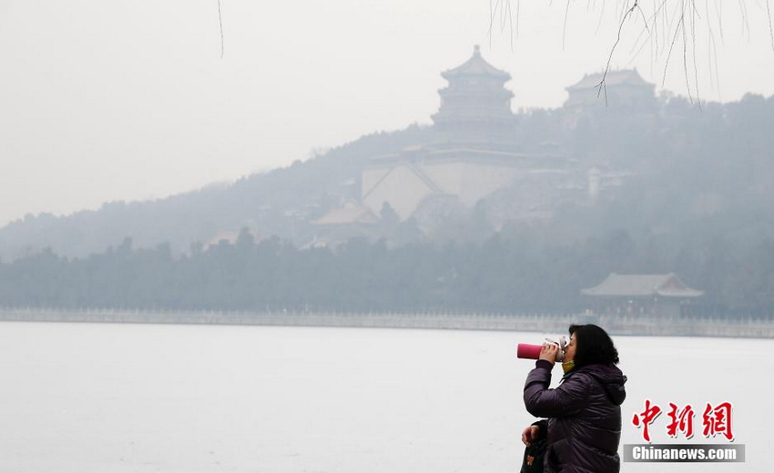 月14日，一名游客在北京颐和园里喝水，昆明湖上蒙上了2015年北京第一场雪，雾霾却将雪景掩盖，远处的景色难以辨清。当日，北京空气陷入重度污染。