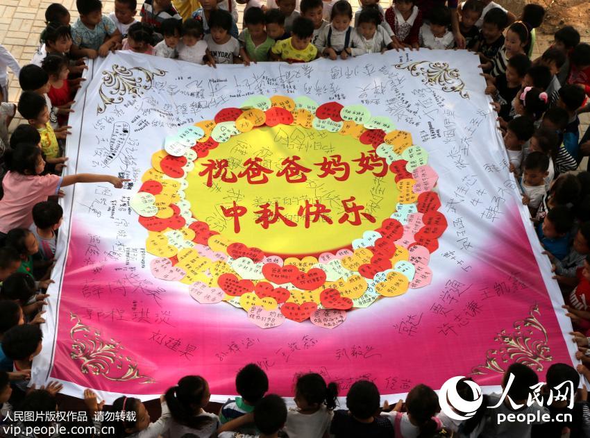 2015年9月23日,河北省广平县明德小学开展以“感恩中秋节、祝福送亲人”为主题的中秋节感恩教育活动,留守儿童们亲手制作中秋节贺卡,写上对爸爸妈妈的中秋节祝福语,并用贺卡拼出“爱心大月饼”,表达对在外打工父母的思念和感恩之情。(程学虎/人民图片)