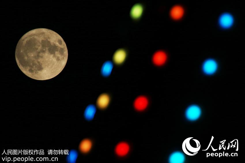 11月14日，山东省烟台市上空，“超级月亮”在霓虹灯后方升起。（唐克/人民图片）
