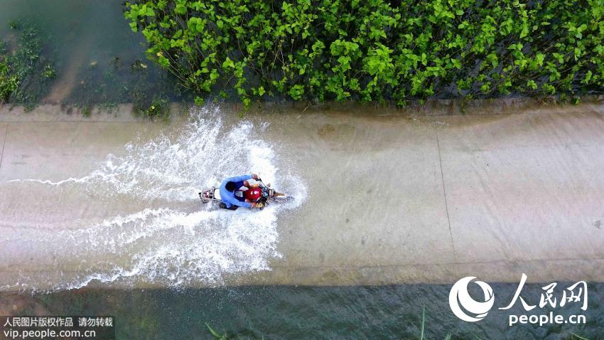 7月12日航拍的广西环江毛南族自治县水源镇被洪水淹没的道路上骑行。