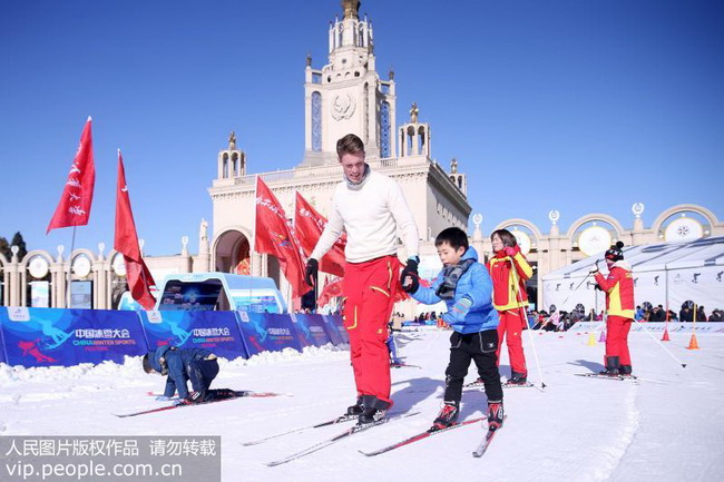 2018年12月23日，世锦赛三连冠的挪威运动员指导小朋友滑雪。