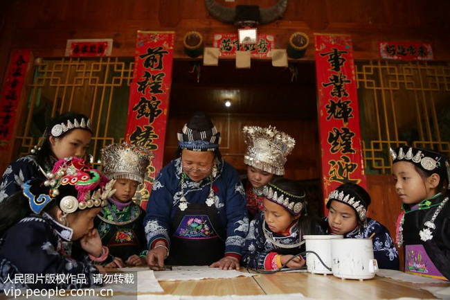 12月23日，在贵州省丹寨县排调镇也改村远景自然寨，“苗族蜡染”非遗传承人王阿板（中）给孩子们示范蜡染绘画技艺。
